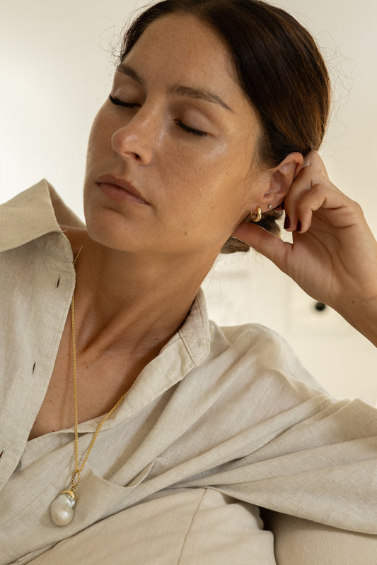 Woman wearing a gold necklace and earring, resting on her hand