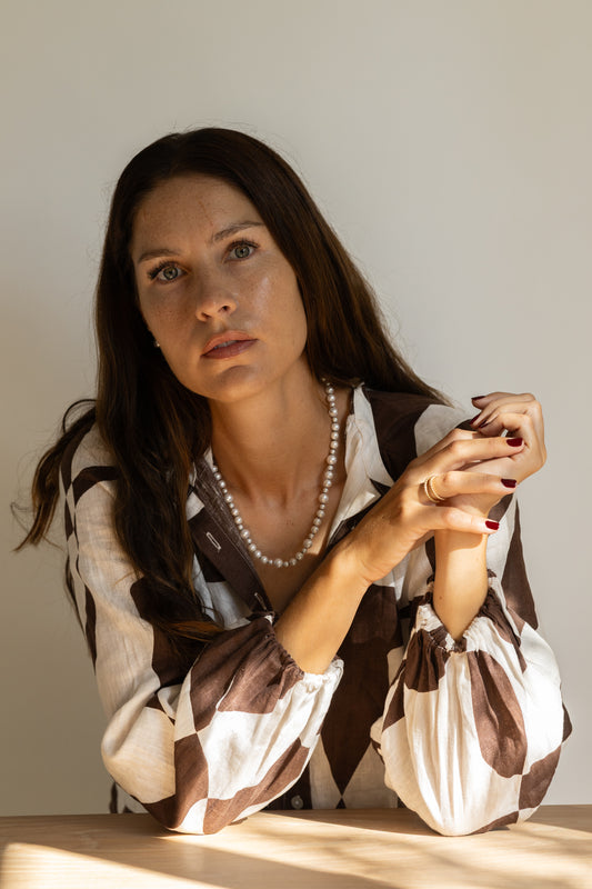 Woman wearing a patterned blouse with a pearl necklace against a neutral background