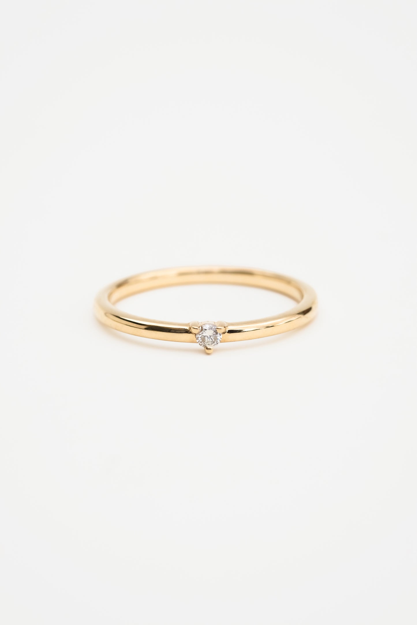 A gold band ring with a single round diamond on it, displayed against a white background.