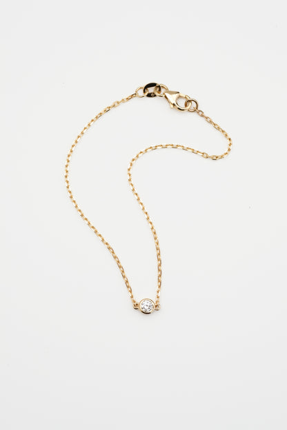 Gold bracelet with a round diamond, displayed on a white background.