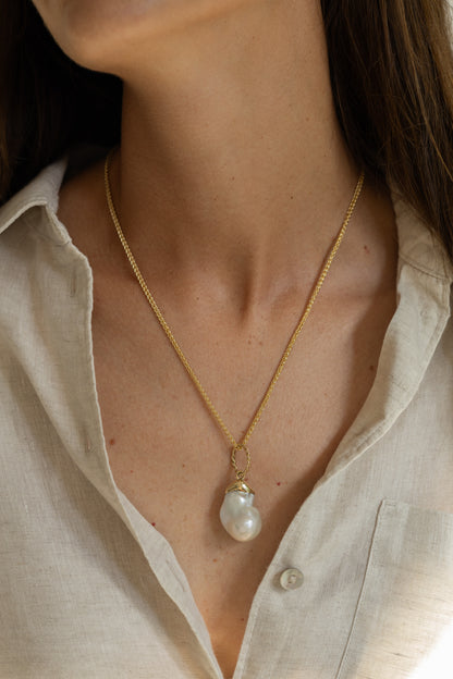Gold necklace with a pearl pendant worn by a person in a light-colored shirt.