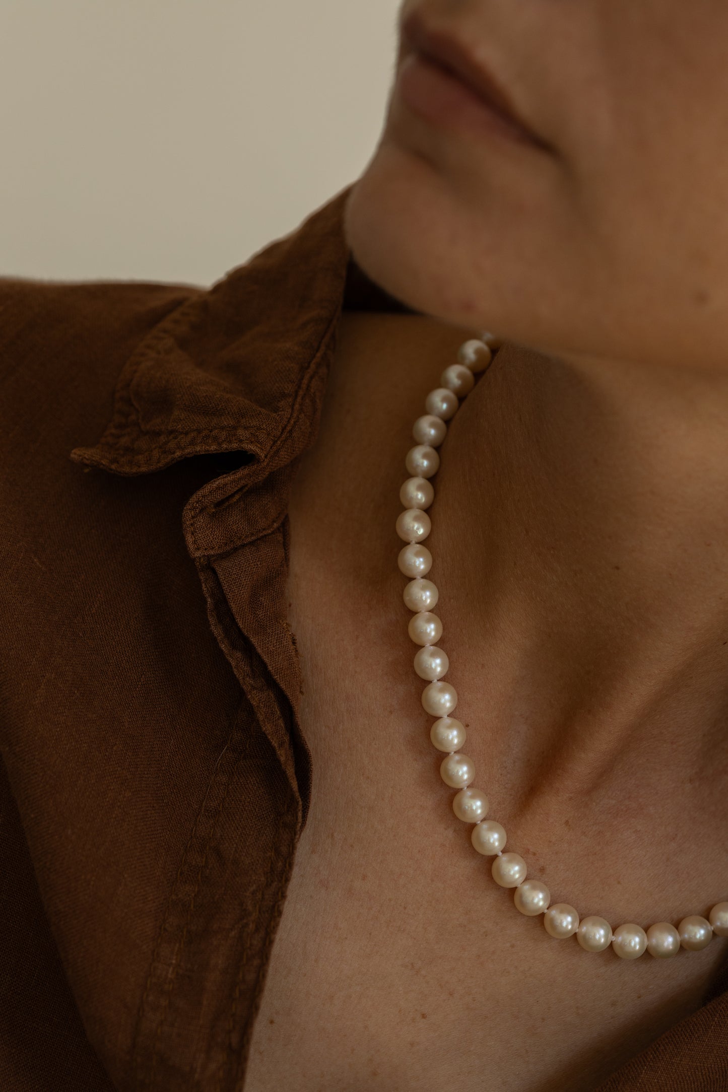 Pearl necklace worn by a person with a brown shirt against a neutral background