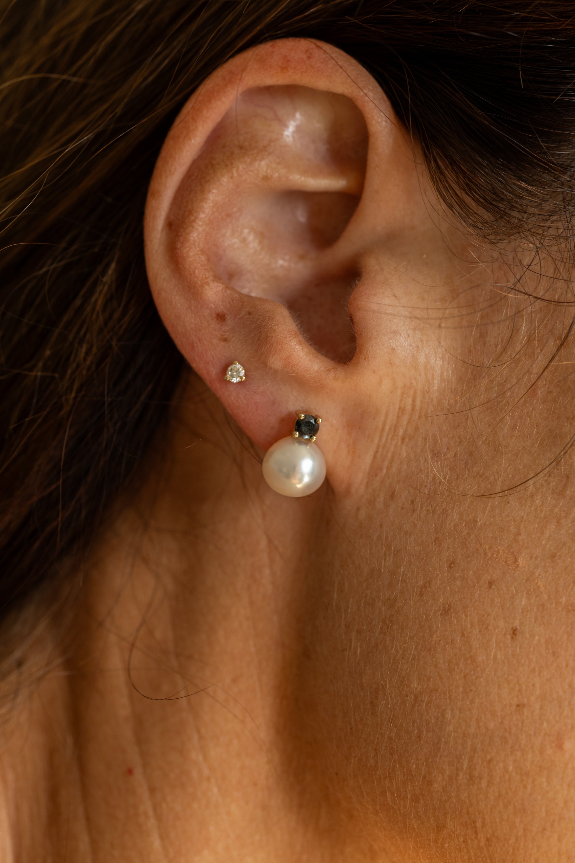 Close-up of an ear wearing two earrings: a pearl and a small diamond.