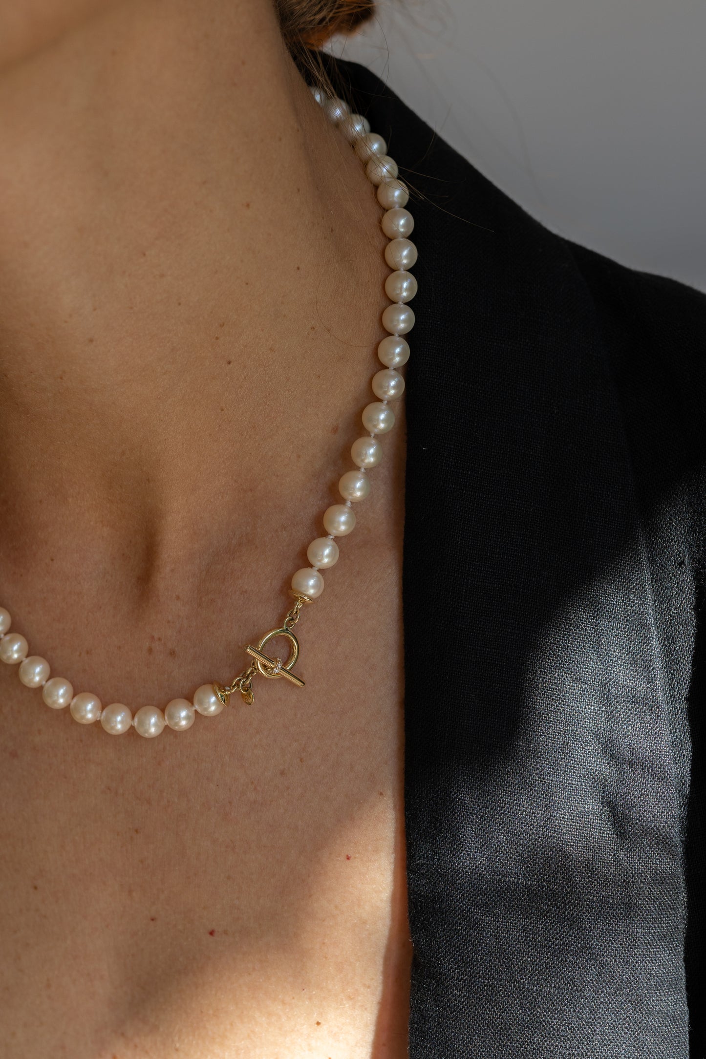 Pearl necklace with a gold clasp worn by a person against a neutral background