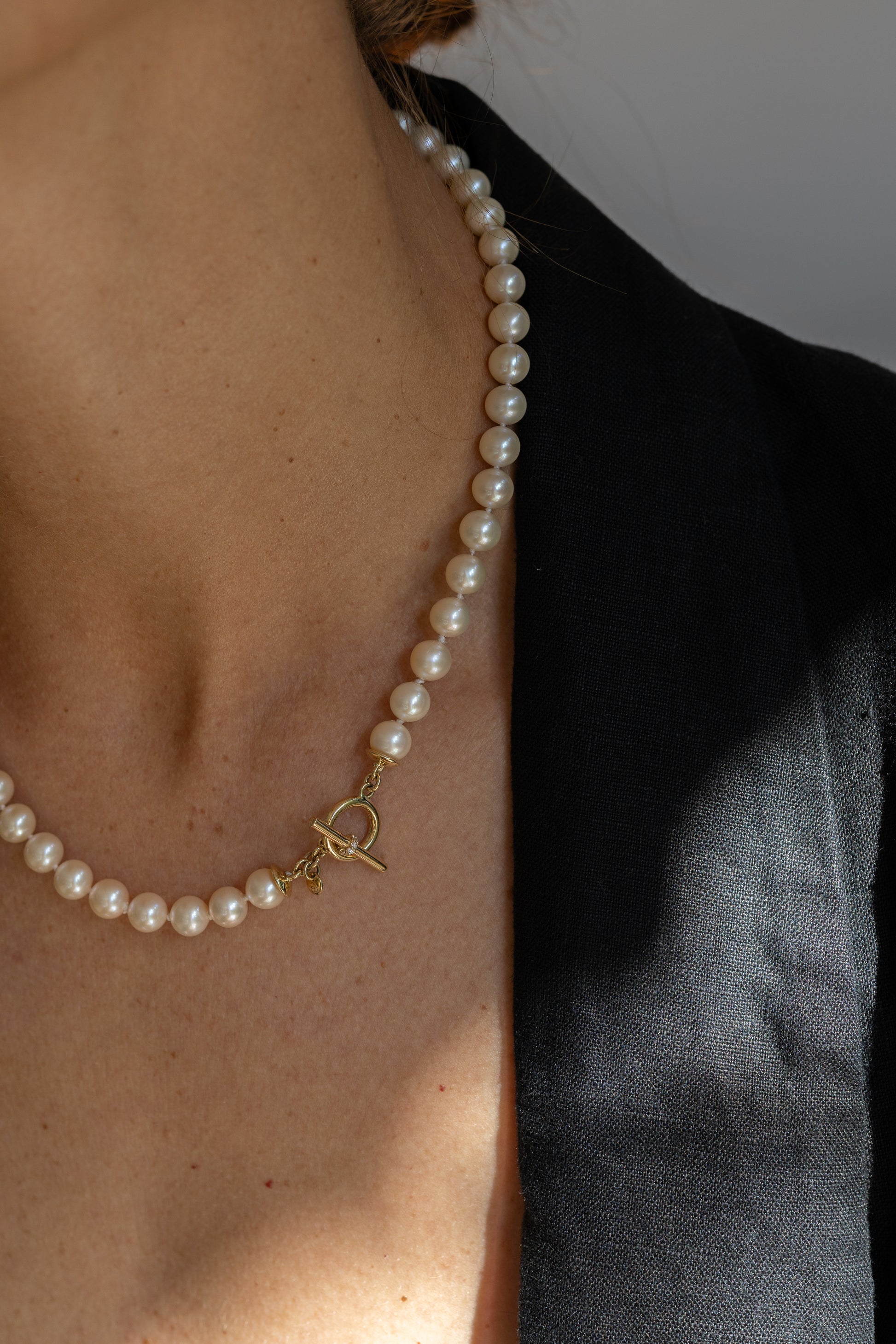 Pearl necklace with a gold clasp worn by a person against a neutral background