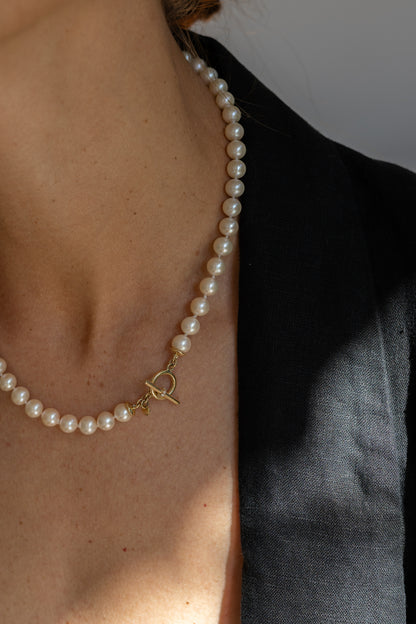 Pearl necklace with a gold clasp worn by a person against a neutral background