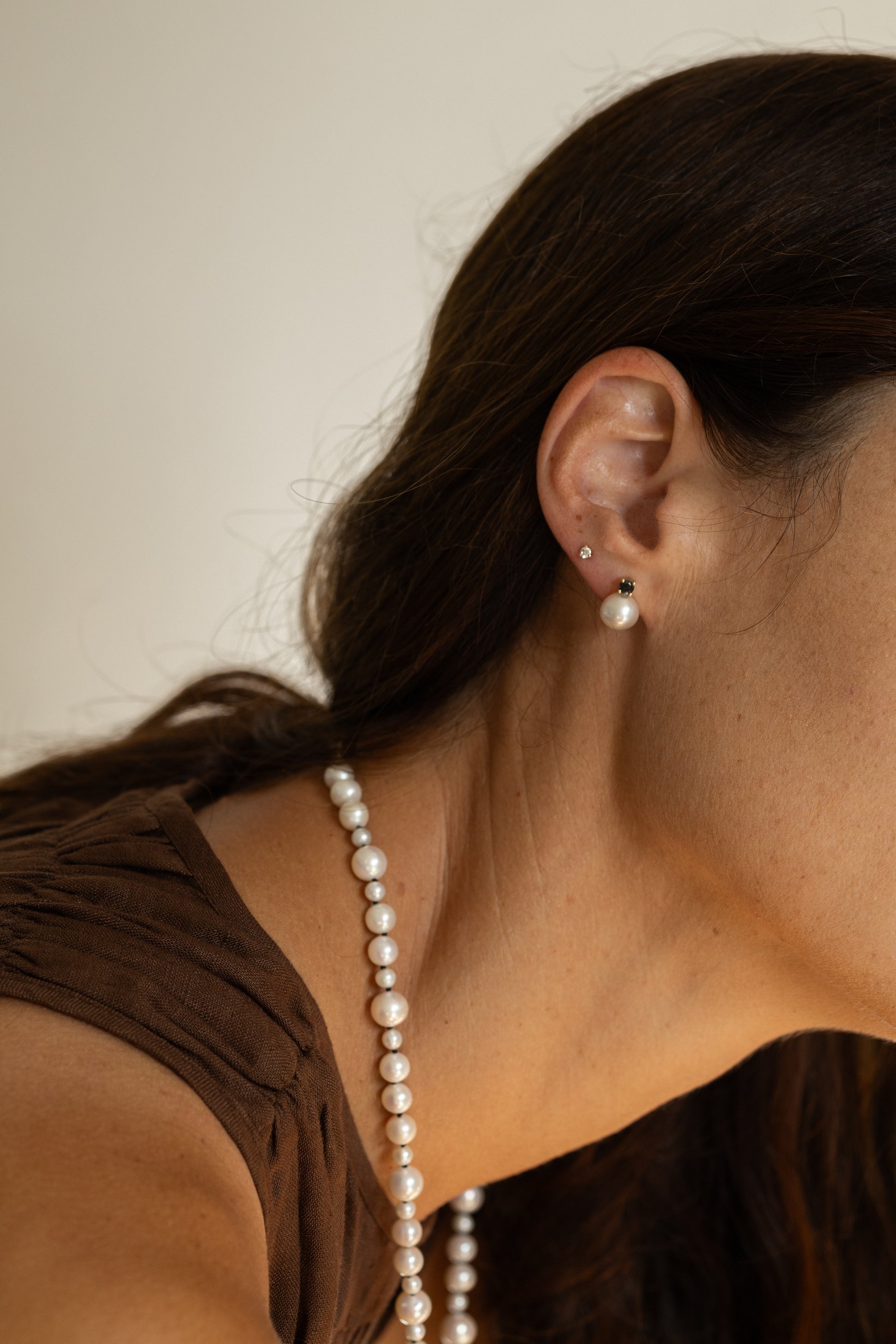 Close-up of a person wearing pearl earrings and a necklace against a neutral background