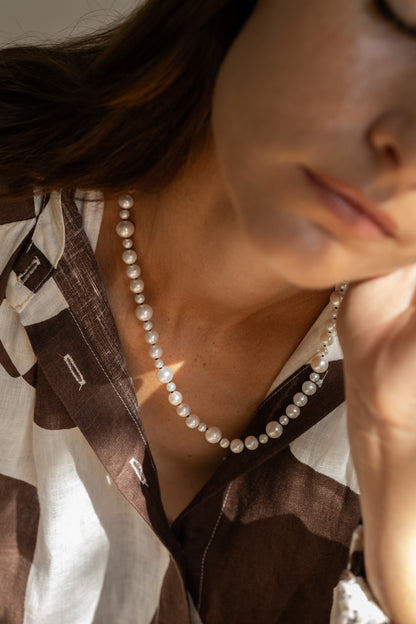 Close-up of a person wearing a pearl necklace with a blurred background