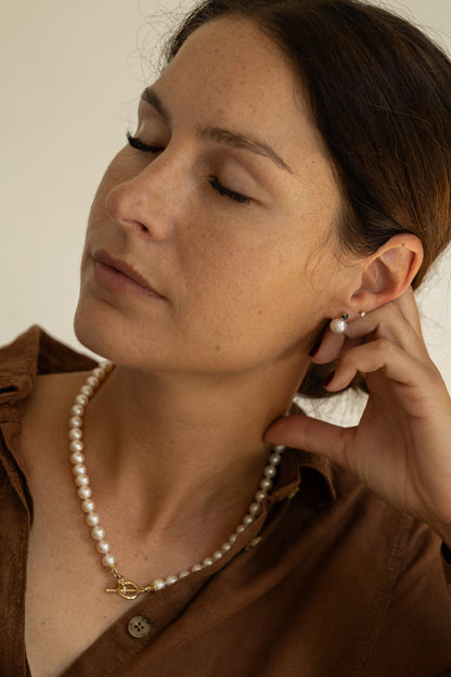 Woman wearing a pearl necklace and earrings, resting on her hand